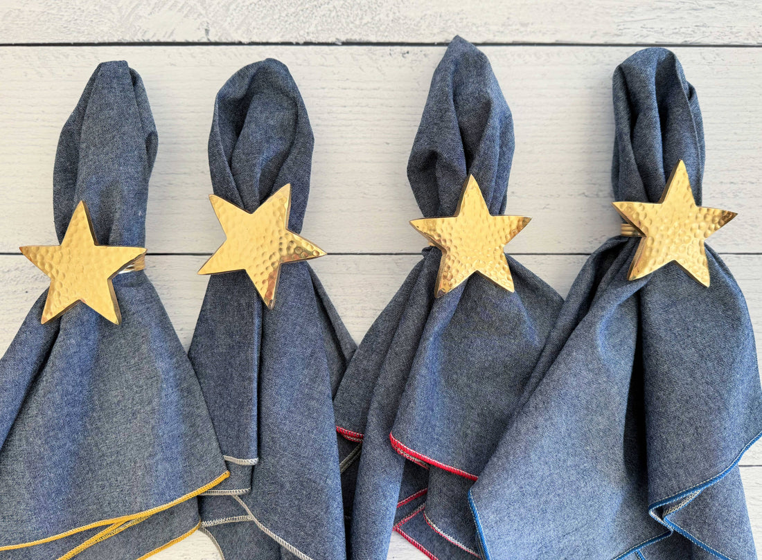 Four denim napkins with gold star napkin rings on a wooden surface