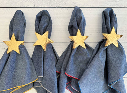 Four denim napkins with gold star napkin rings on a wooden surface