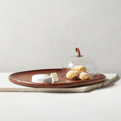 Acacia wood tray with cheese and pastries under a glass cloche on a light surface.