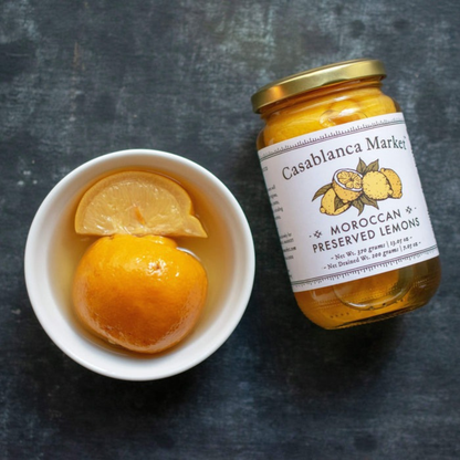 Jar of Casablanca Market Moroccan Preserved Lemons next to a bowl with preserved lemons on a dark surface