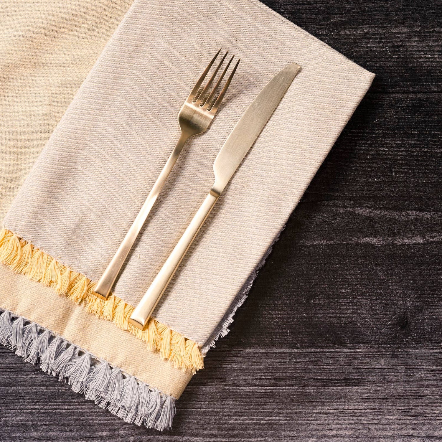 Gold fork and knife on a beige napkin with gold trim on a dark wooden surface