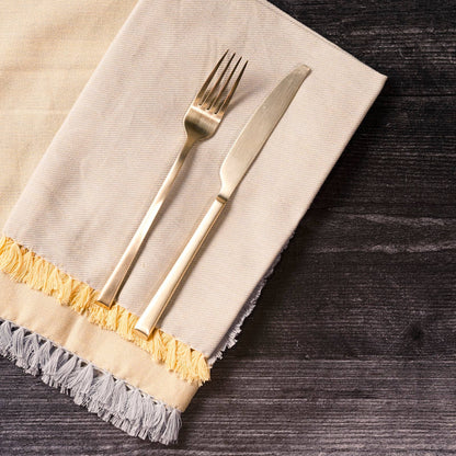 Gold fork and knife on a beige napkin with gold trim on a dark wooden surface