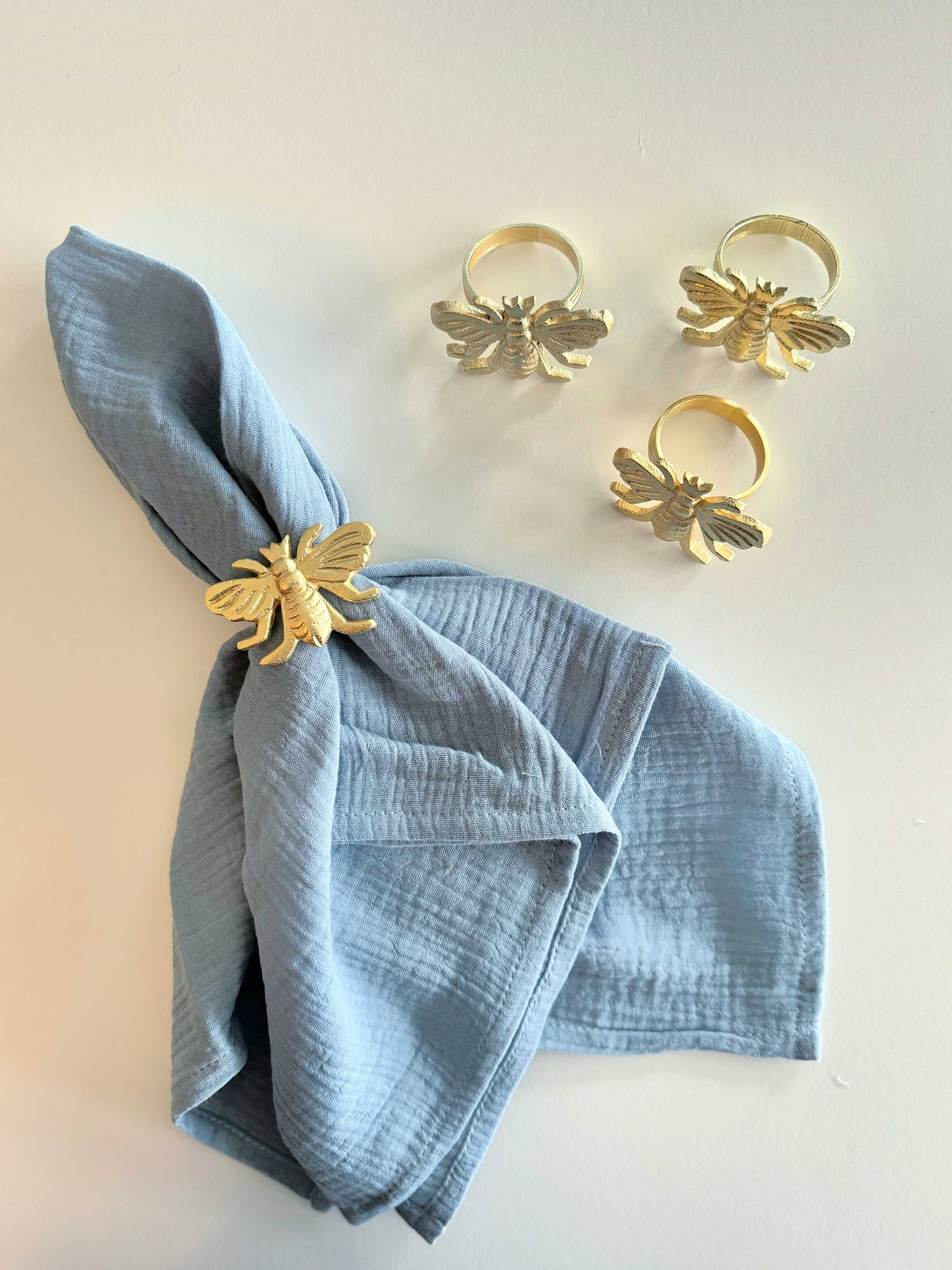 Gold bee-shaped napkin rings on a blue napkin against a white background