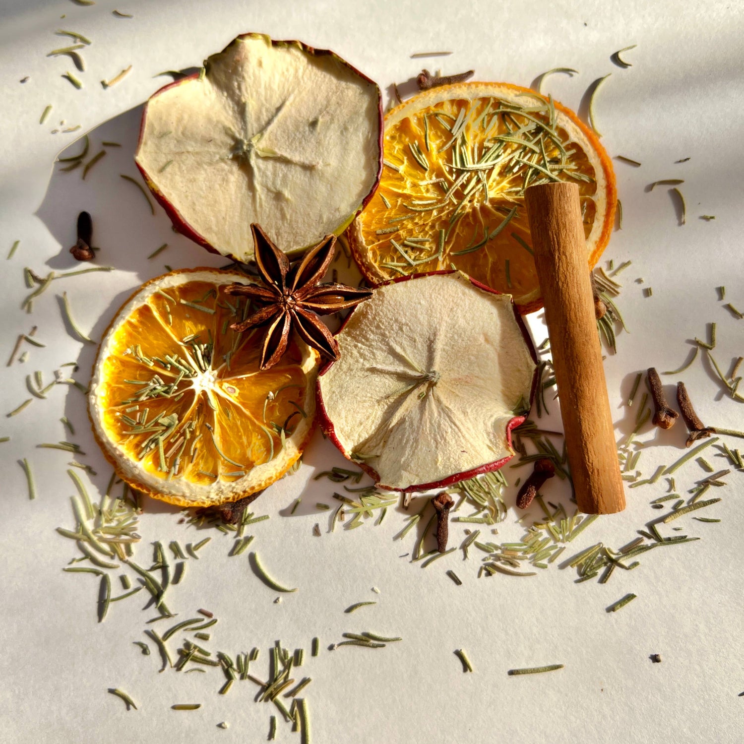 Spices and herbs including cinnamon sticks, star anise, and orange slices on a white surface.