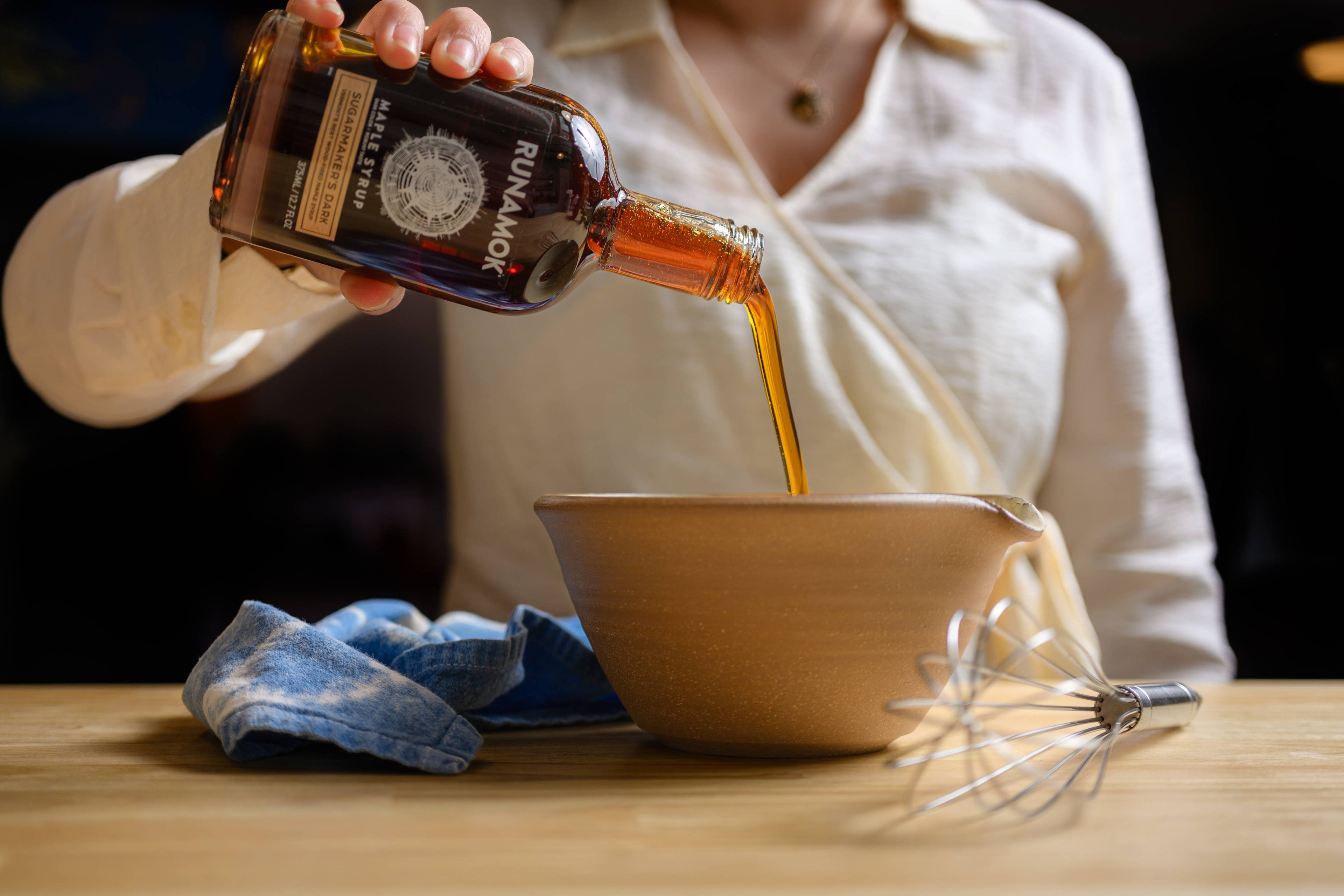 Person pouring a bottle of Dom Juan into a bowl on a wooden surface.