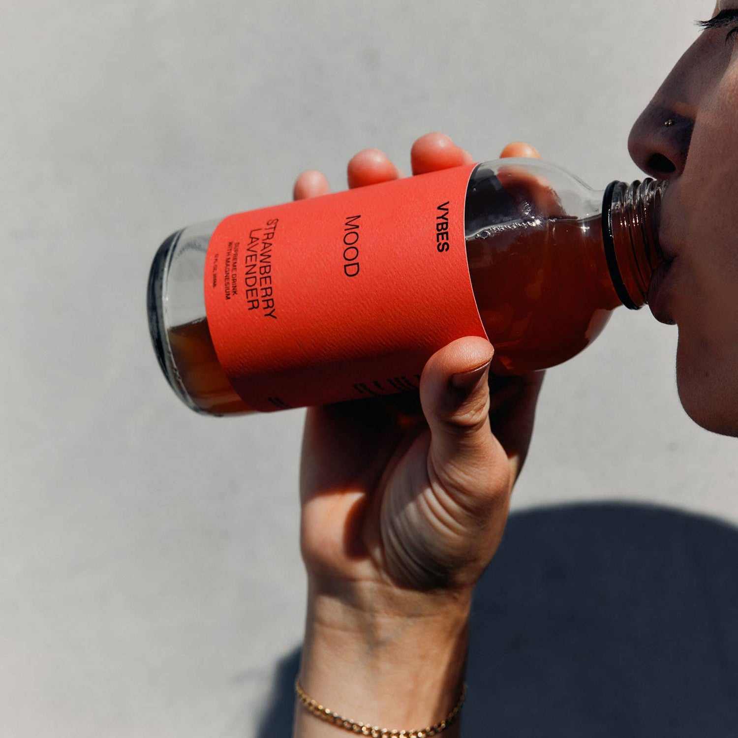 Person holding a red bottle with a straw, drinking from it against a neutral background