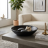 Arendal black mango wood bowl filled with dark and light stones, styled on a concrete coffee table in a modern living room setting.