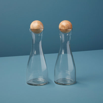 Two clear glass cruets with wooden tops on a blue background