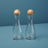 Two clear glass and mango wood cruets with wooden tops on a blue background