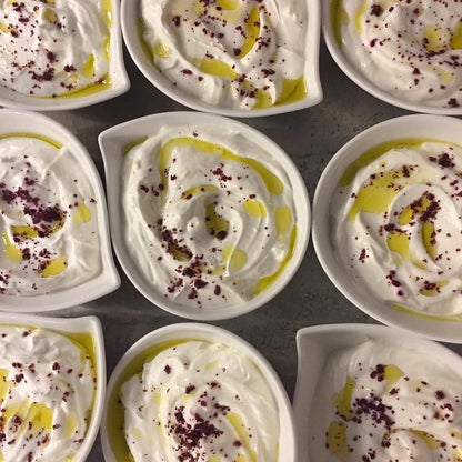Multiple small bowls filled with hummus garnished with cured sumac and olive oil.