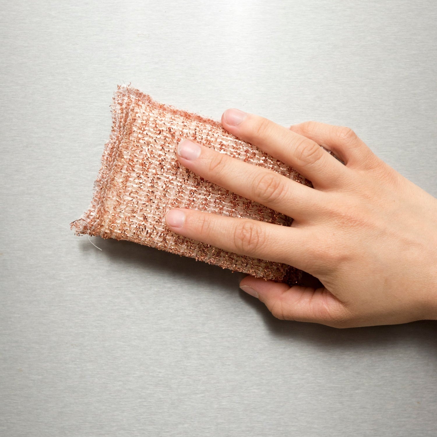 Hand holding a pink textured sponge on a gray background