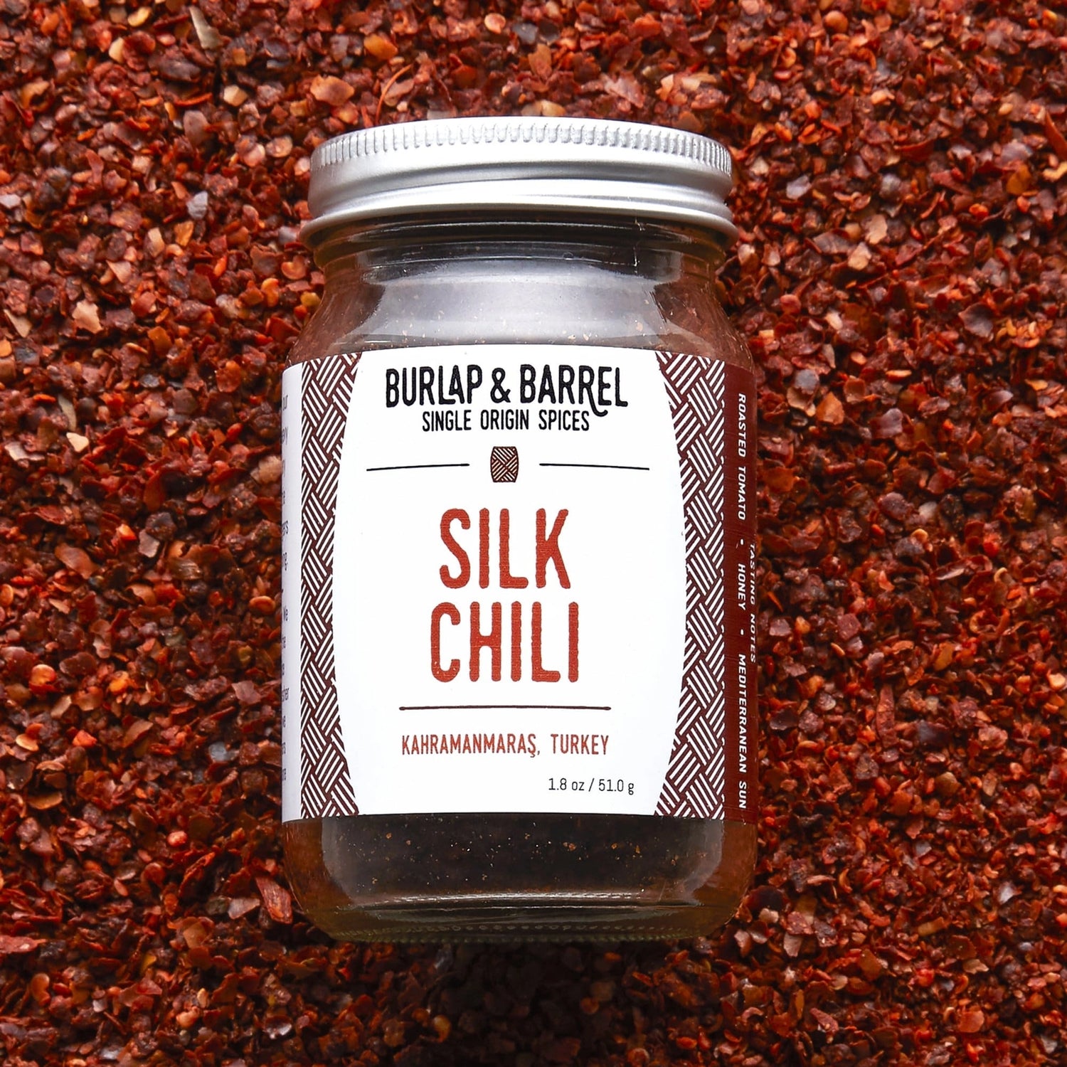 Jar of Burlap &amp; Barrel Silk Chili spice on a bed of red chili flakes
