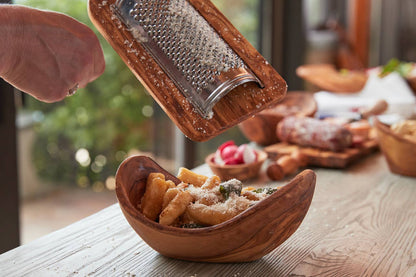 Wooden bowl with food being grated by a hand holding a wooden grater.