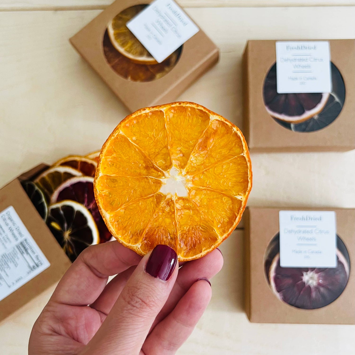 Dried orange slice held by a hand with boxes of dried fruits in the background.