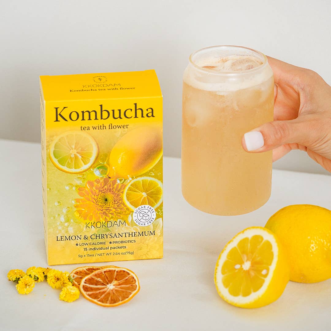 Kombucha box with a glass of lemon-flavored drink, lemons, and flowers on a white background
