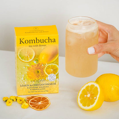 Kombucha box with a glass of lemon-flavored drink, lemons, and flowers on a white background