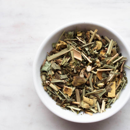 White bowl filled with dried herbs on a light marble background