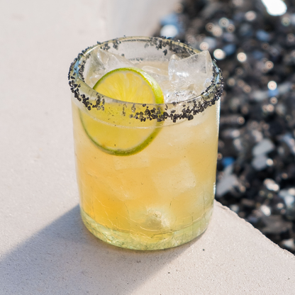 Yellow cocktail with lime wedge and blackberry salt rim 