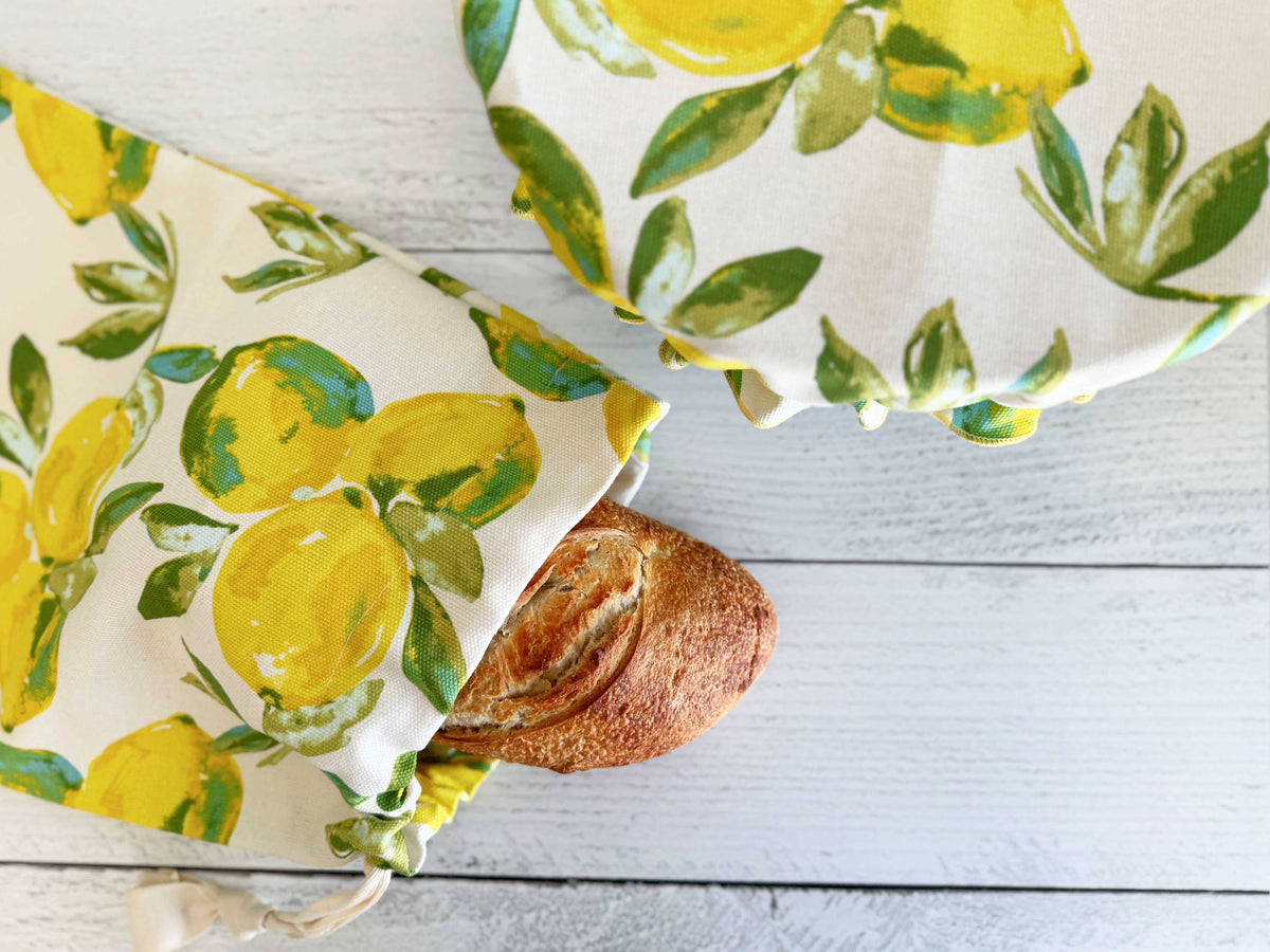 A bowl cover and bread bad with fresh bread in it, in a lemon pattern