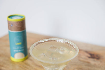 A cocktail rimmed with lime salt in the foreground, with a blurred container of the rimming salt in the background