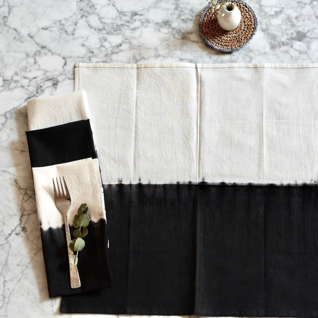 Black and white placemat with a napkin featuring cutlery and eucalyptus on a marble surface.