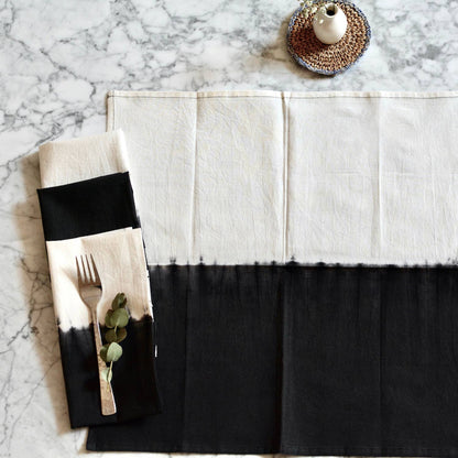 Black and white placemat with a napkin featuring cutlery and eucalyptus on a marble surface.
