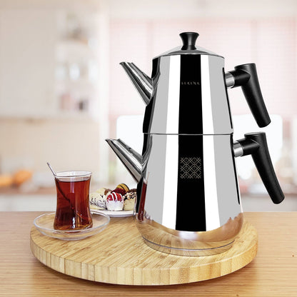 Stainless steel espresso maker on a wooden tray with a glass of tea and snacks in the background.