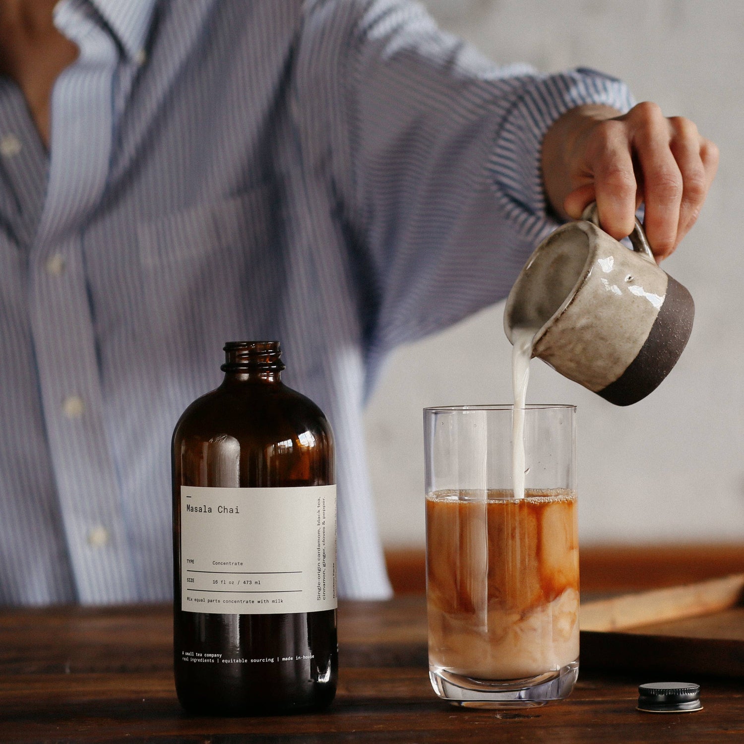 Person pouring liquid from a bottle into a glass on a wooden surface.