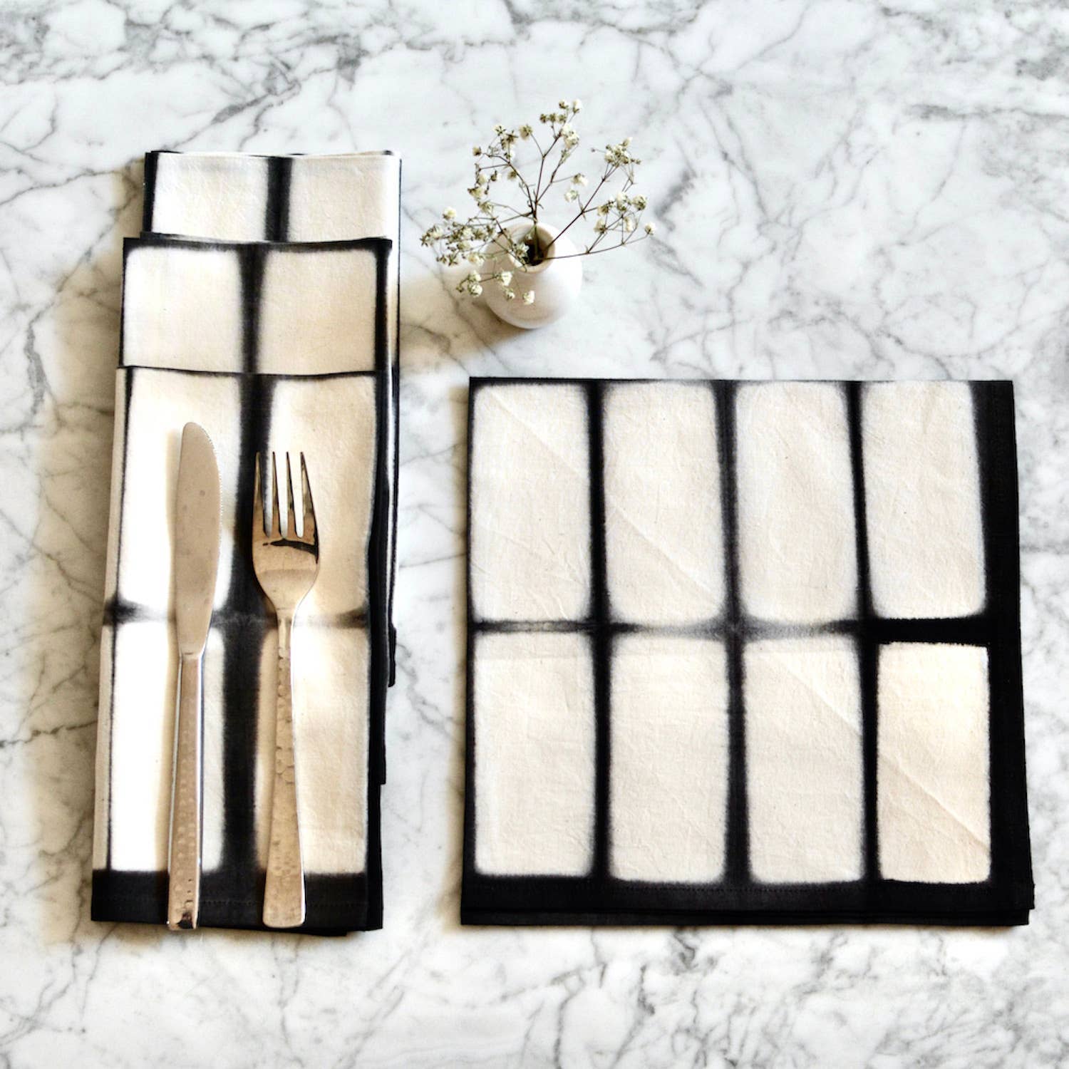 Folded black and white place mat with cutlery on a marble surface