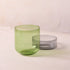 Two glass tumblers, one green and one gray, on a light surface with a neutral background