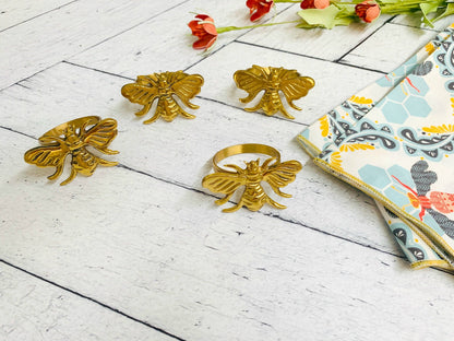 Gold bee-shaped napkin rings on a white wooden surface with honey bee cloth napkins