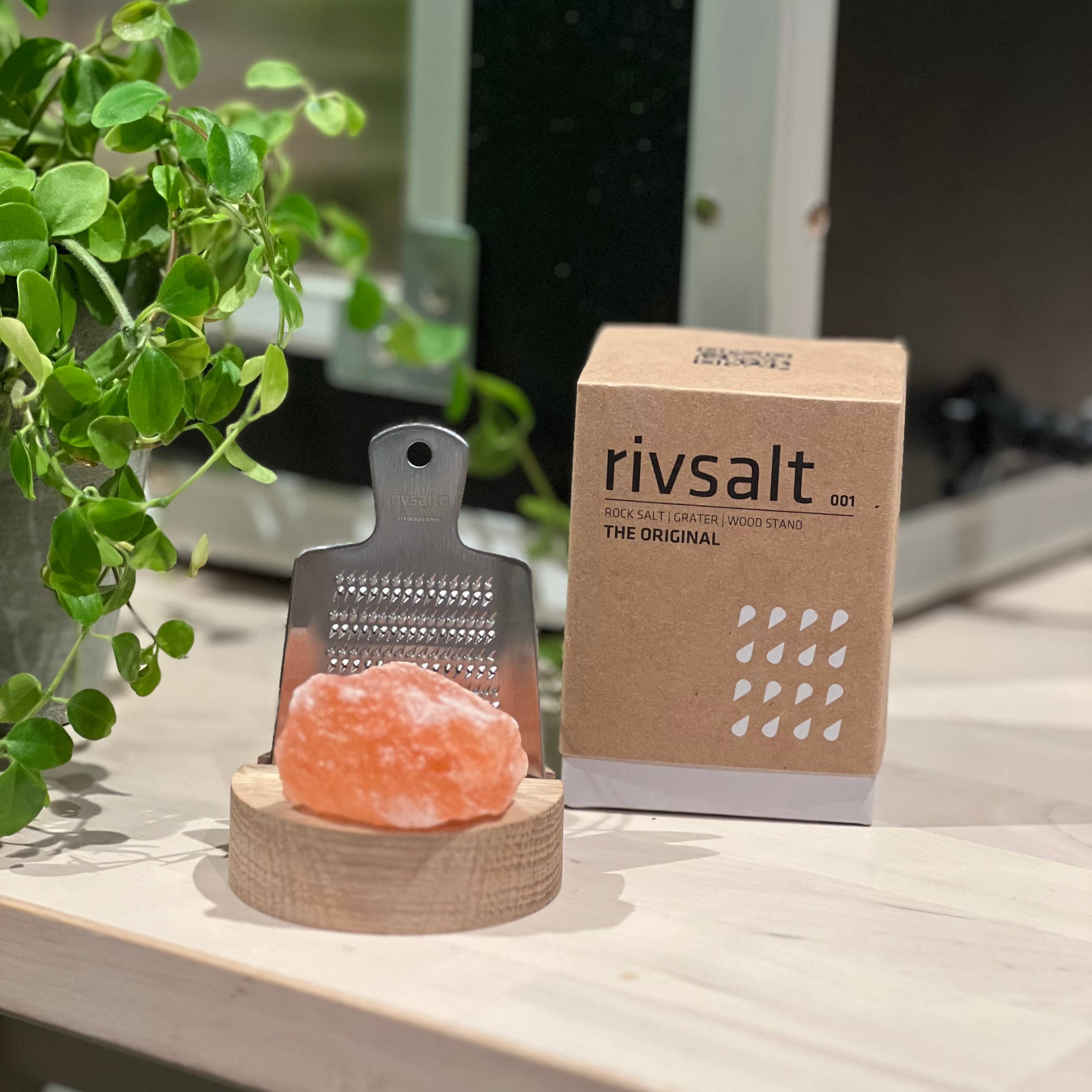 Rivsalt Himalayan salt lamp with packaging on a wooden surface with a plant in the background