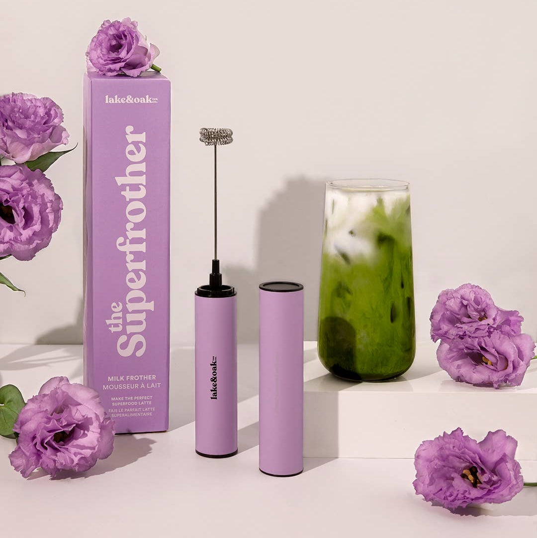 Purple milk frother with packaging and flowers on a light background