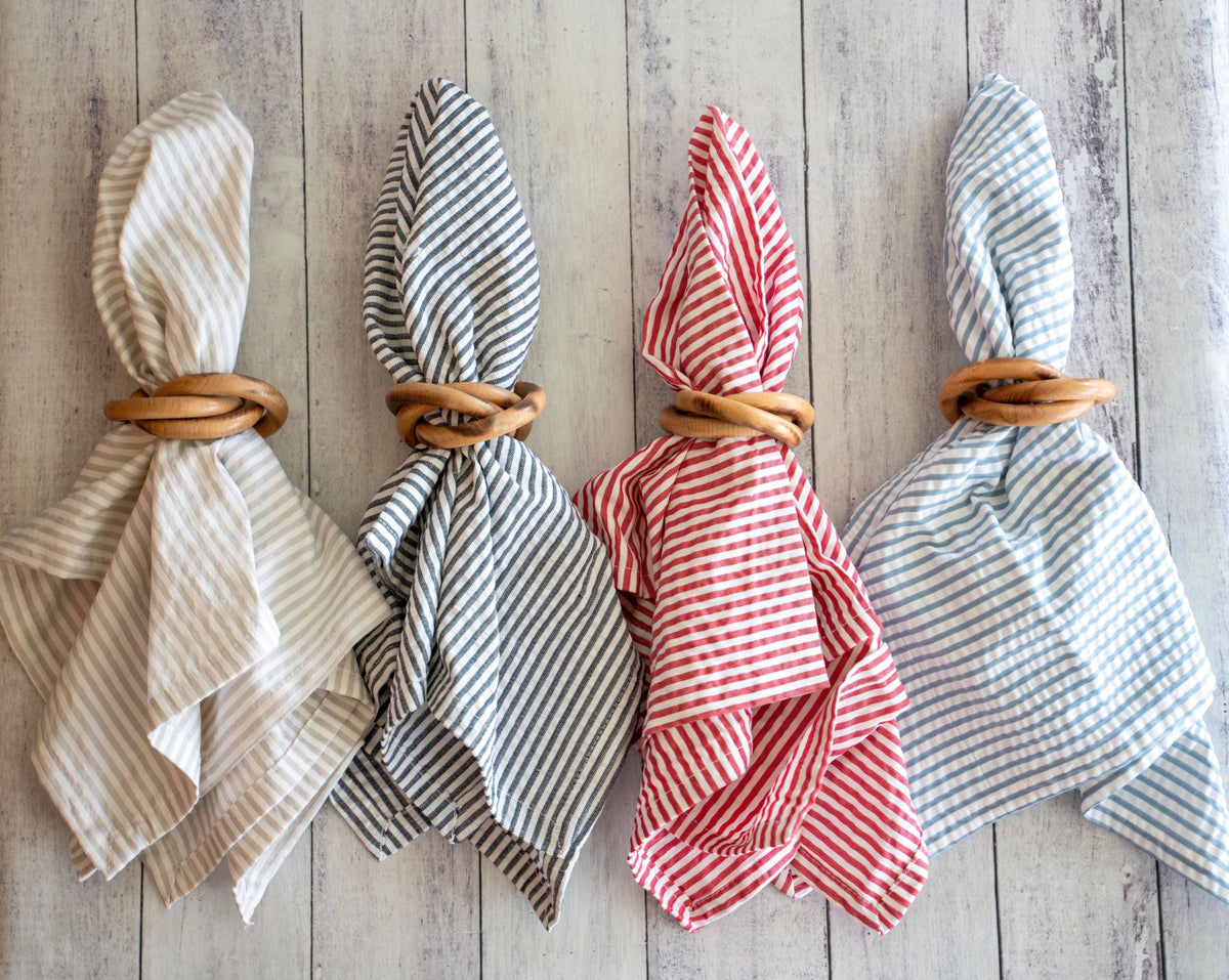 Four folded napkins with wooden bangles napkin rings on a wooden surface