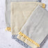 Three textured towels with frayed edges in gray, beige, and yellow on a light gray background.