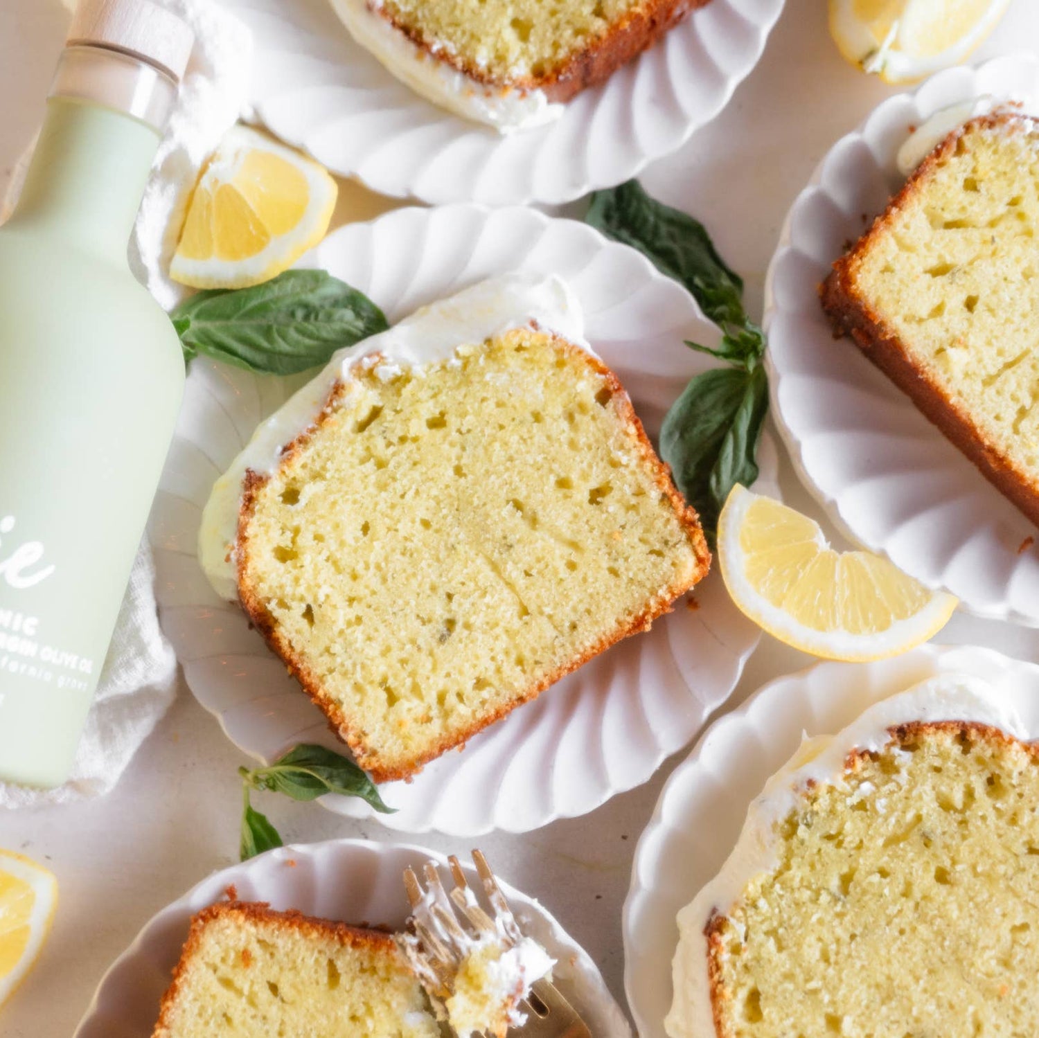 Slices of lemon cake on white plates with lemons and a bottle labeled &