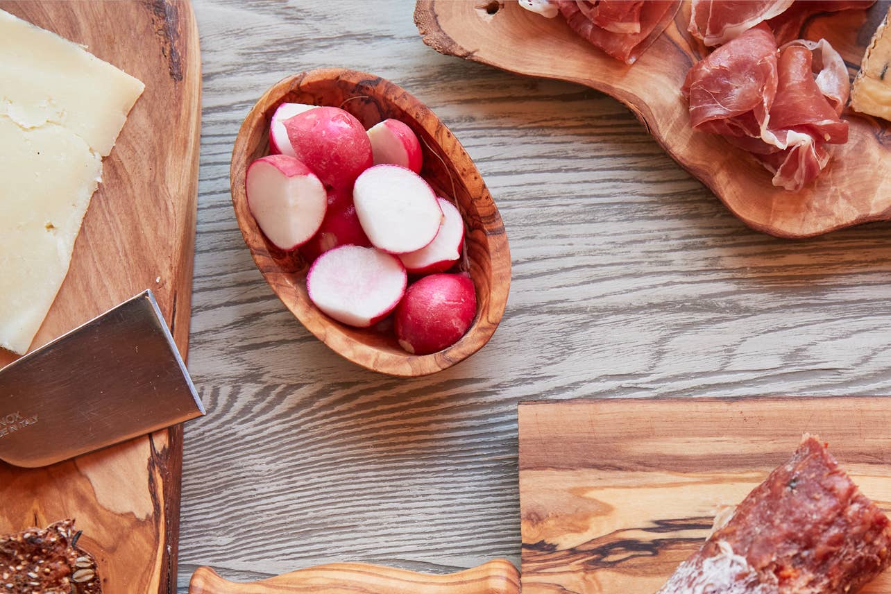 Italian Olivewood Aperitivo Bowl filled with radishes with meat platters in the background