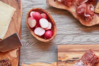 Italian Olivewood Aperitivo Bowl filled with radishes with meat platters in the background