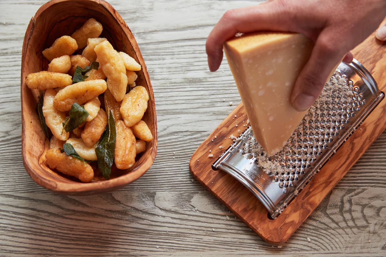 Bowl of pasta with a block of cheese and grater on a wooden surface