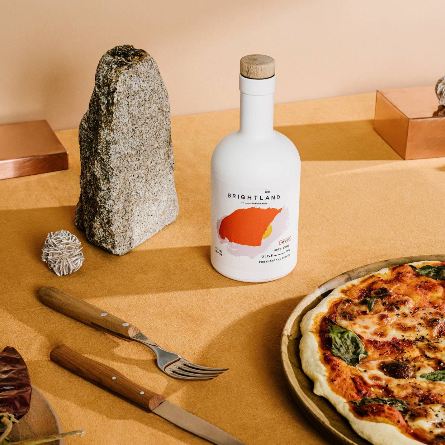 Bottle of Brightland olive oil on a table with a pizza and cutlery