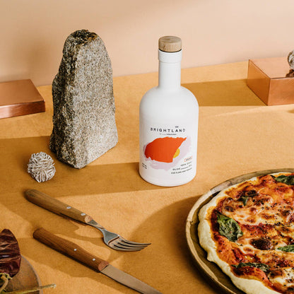 Bottle of Brightland olive oil on a table with a pizza and cutlery