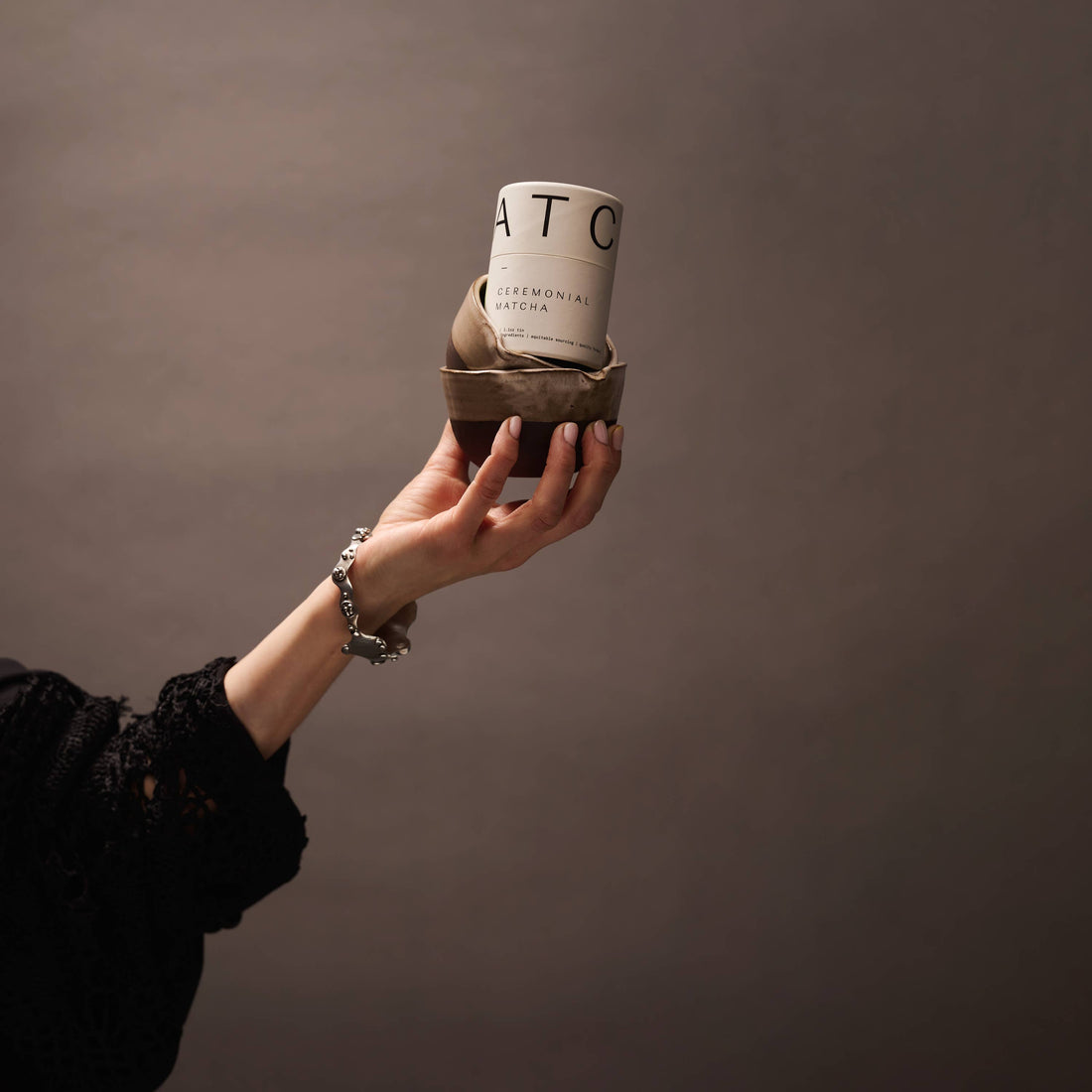 Hand holding a small ceramic cup with a textured surface against a plain background