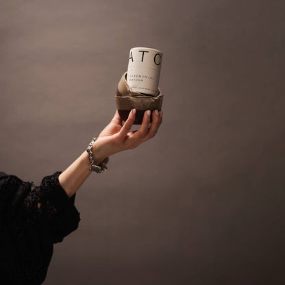 Hand holding a small ceramic cup with a textured surface against a plain background