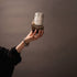 Hand holding a small ceramic cup with a textured surface against a plain background