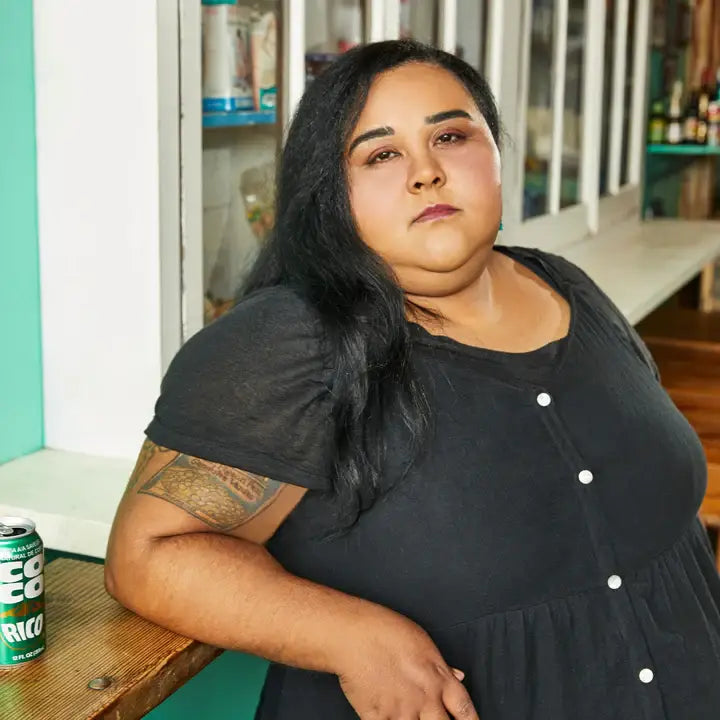 Woman in a black dress sitting at a table with a can of Fanta Ricci in a casual setting.