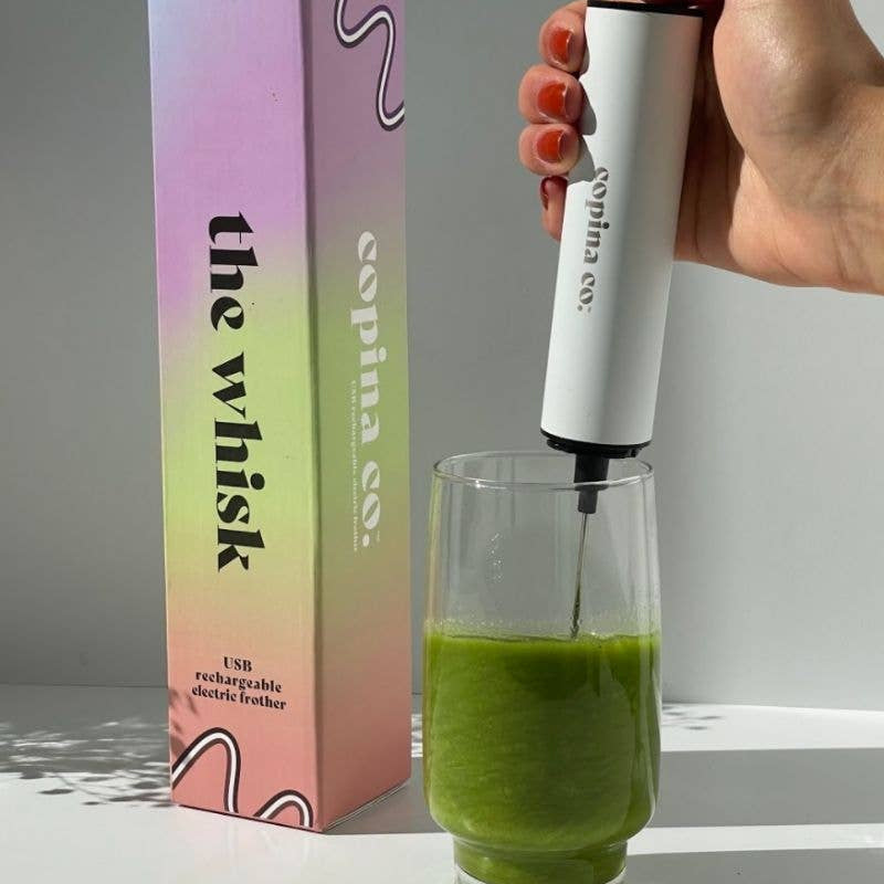 Copina Co. whisk being used to mix a green drink with its packaging in the background.