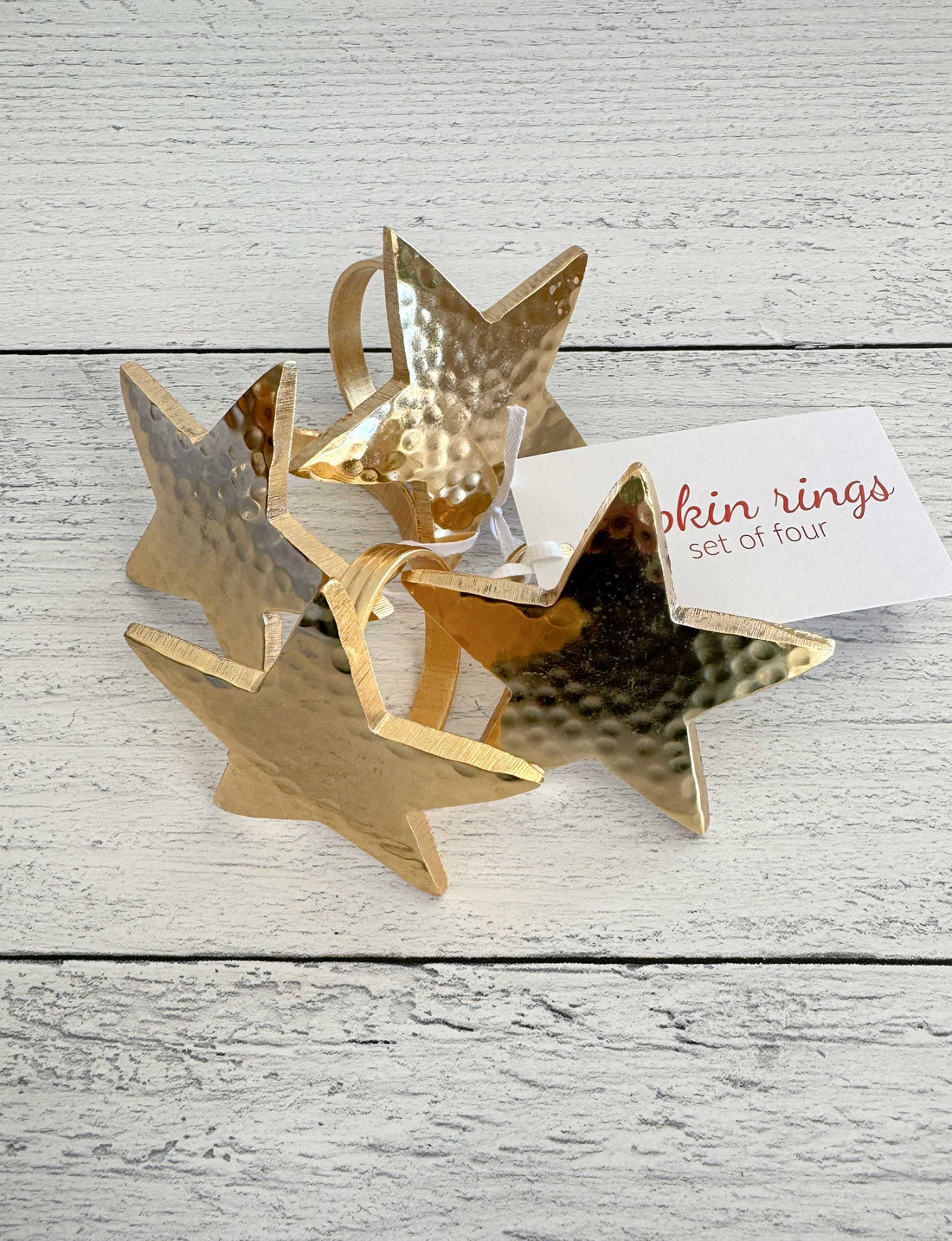 Set of four gold star-shaped napkin rings on a wooden surface with a card.