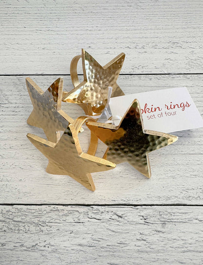 Set of four gold star-shaped napkin rings on a wooden surface with a card.