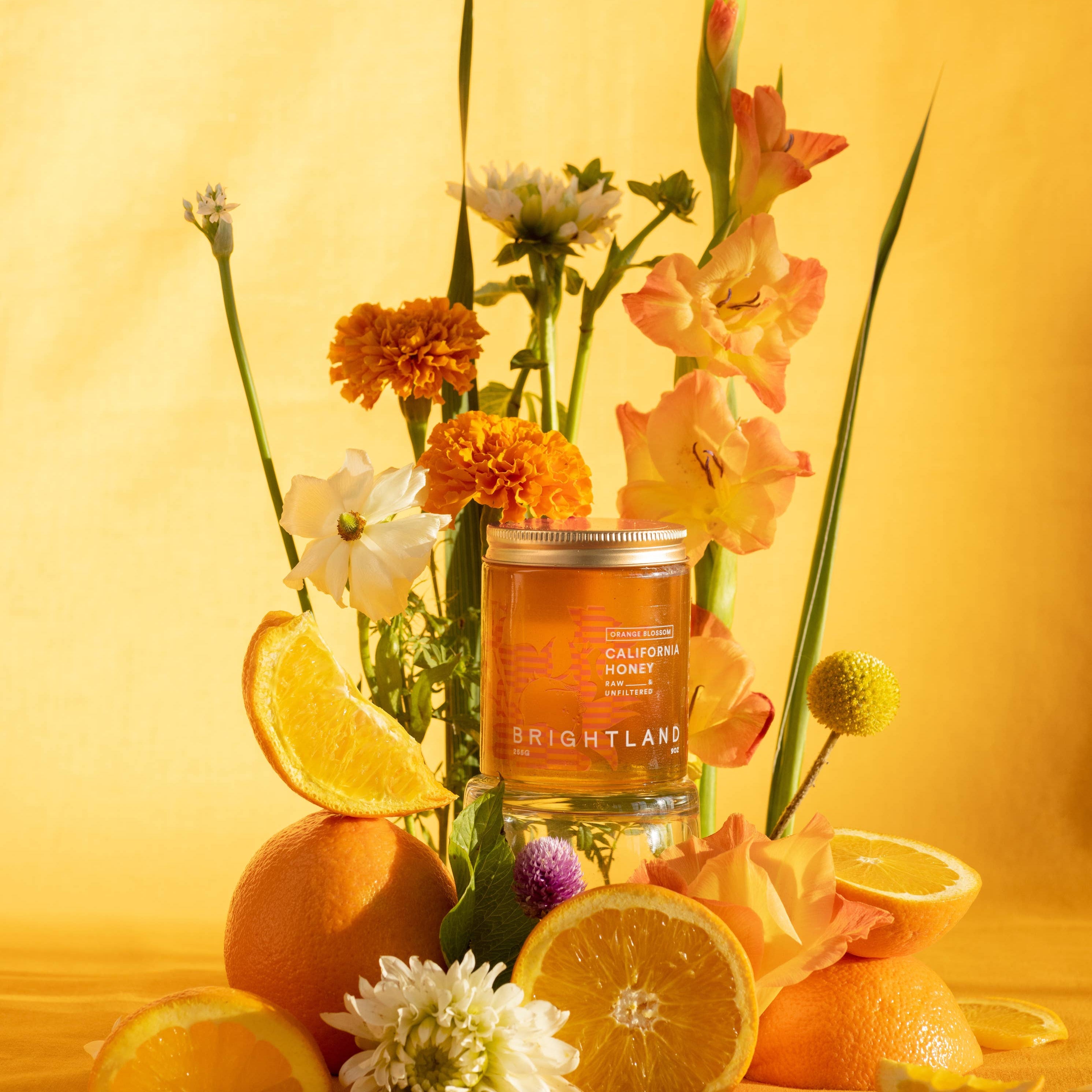 Candle in a glass jar surrounded by lemons, oranges, and flowers on a yellow background