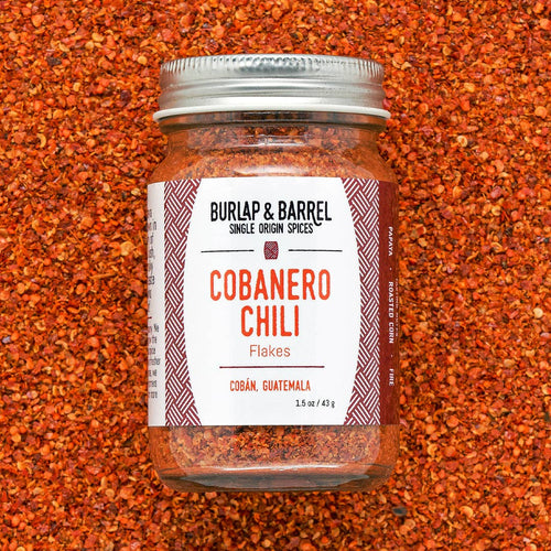 Jar of Burlap & Barrel Cobanero Chili Flakes on a textured red background